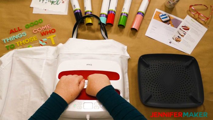 Pressing a silver tote bag with a Cricut EasyPress 2 to create a layered iron on vinyl bag