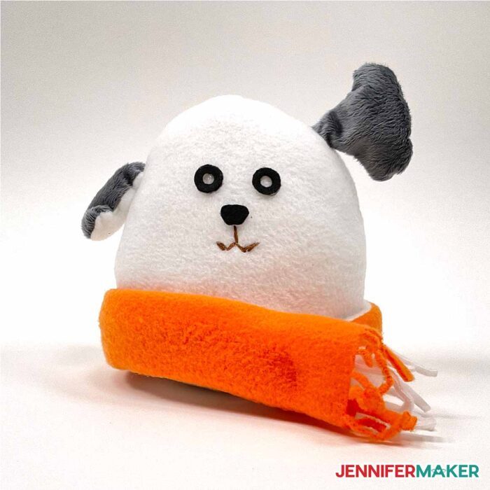 A stuffed cute plushie dog in white fleece with gray ears and an orange scarf.