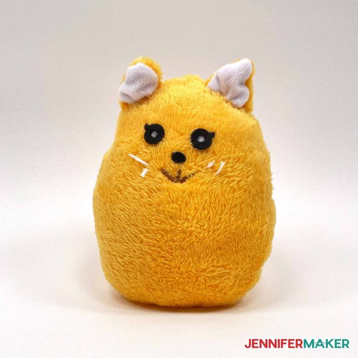 A stuffed cute plushie cat in yellow fleece with sewn and felt details.