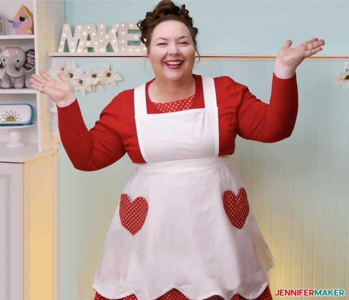 Jennifer Maker wearing a white vintage style apron with red heart-shaped pockets in her craft room.