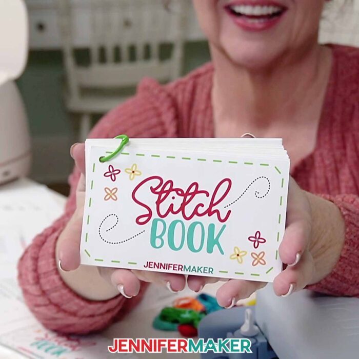 Jennifer Maker holds up her embroidery stitch book with the 'Stitch Book' cover facing forward