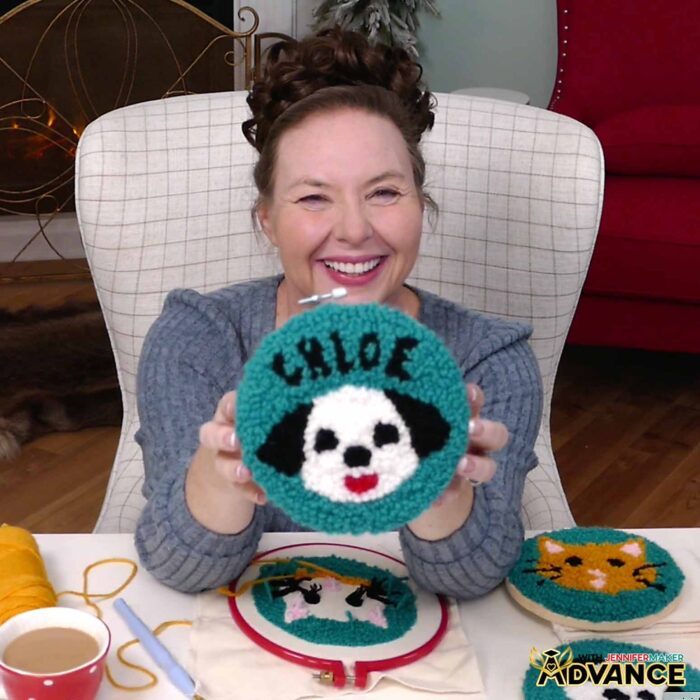 Jennifer holds up a custom punch needle project: a black and white dog with the name "Chloe" on a teal background.