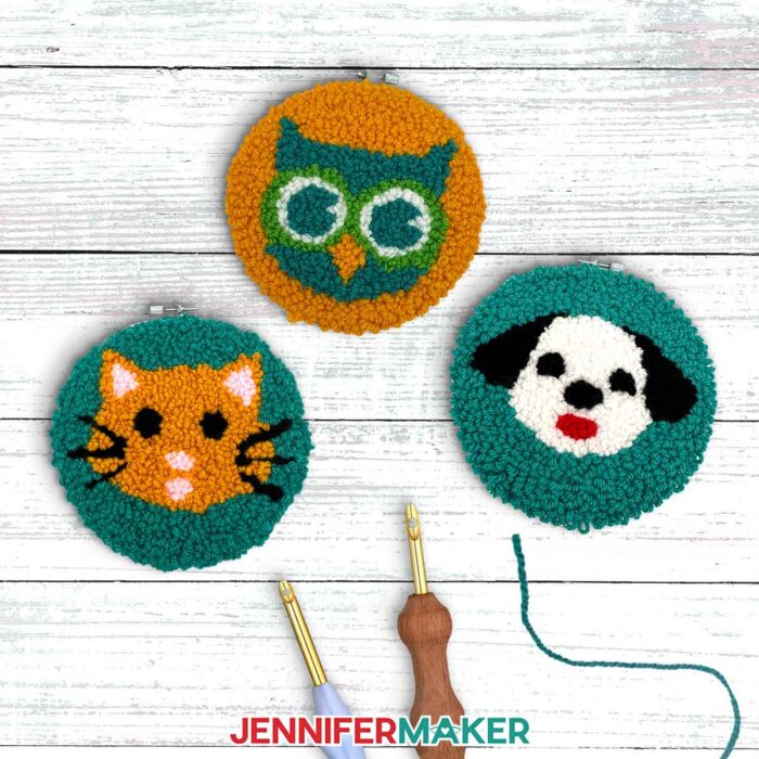 Three punch needle projects on a wooden table: An orange cat with black whiskers, a teal owl with green eyes, and a black and white dog with a red mouth.