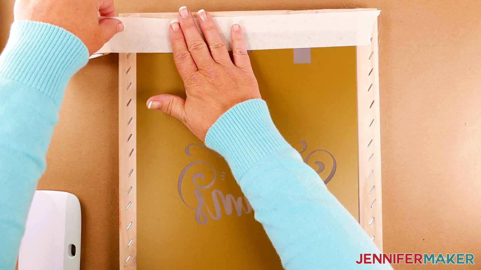 Applying painter's tape to the top of a silk screen with a screen printed shirt stencil adhered below. The painter's tape is used to cover any open areas of the screen to prevent ink from getting onto the shirt in those areas.