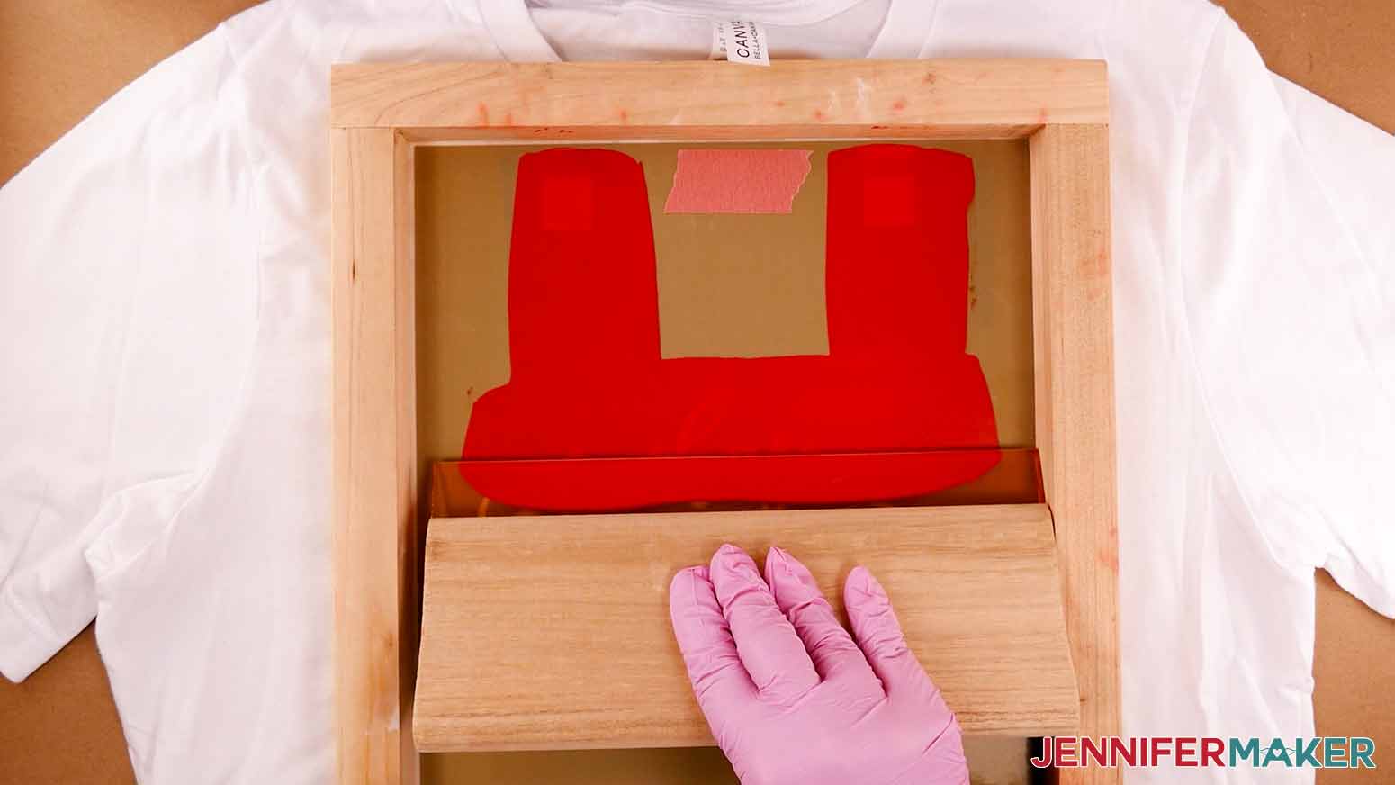 Flooding the prepared screen with red ink using a large squeegee in order to apply the first color to a screen printed shirt