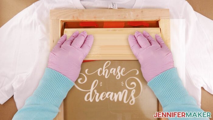 Crafter holding a squeegee on a frame about to pull ink across a stencil for a screen printed shirt.