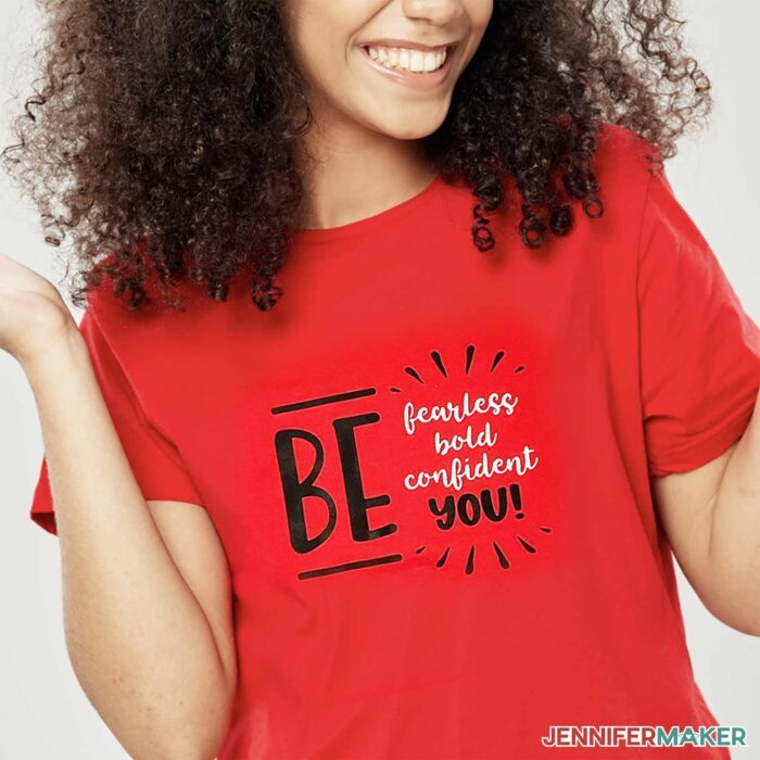 A person wearing a red screen printed shirt with a "Be fearless, bold, confident, you!" design in black and white.