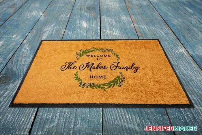 Brown outdoor sublimation doormat with The Maker Family and a wreath on a deck.