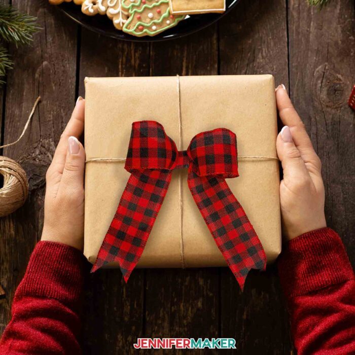 A person holding a gift wrapped in brown paper decorated with a handmade ribbon bow.