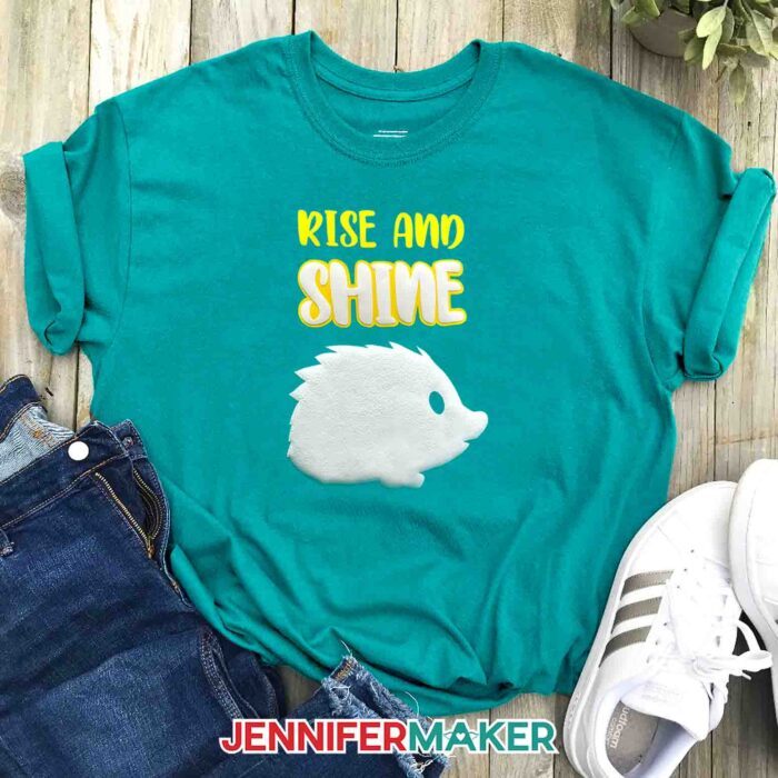 Turquoise blue T-shirt with white puff vinyl porcupine and "Rise and Shine" layered with puff vinyl and yellow HTV. Learn how to make puff vinyl T-shirts with JenniferMaker's tutorial!