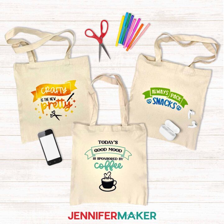Can You Layer Infusible Ink? Learn how with JenniferMaker's tutorial! Three cute tote bags with Infusible Ink designs lay on a white shiplap surface.