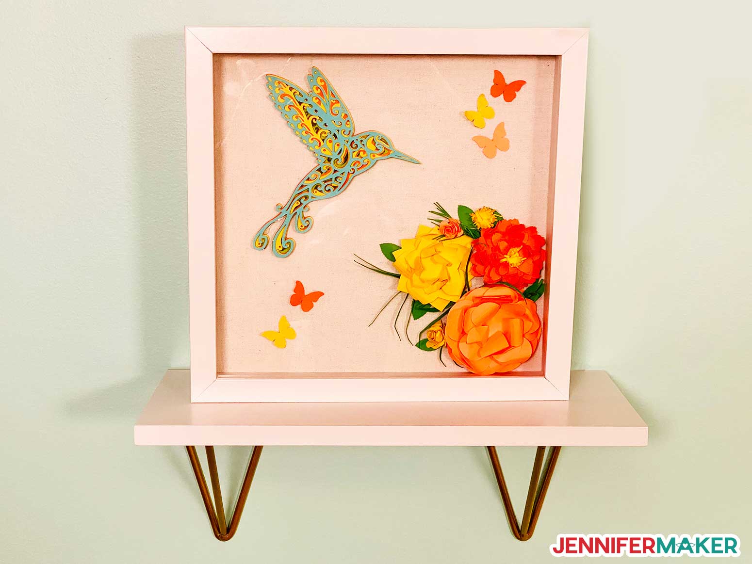 Shadow box with a layered cardstock hummingbird with intricate cuts on Cricut and paper decorations.