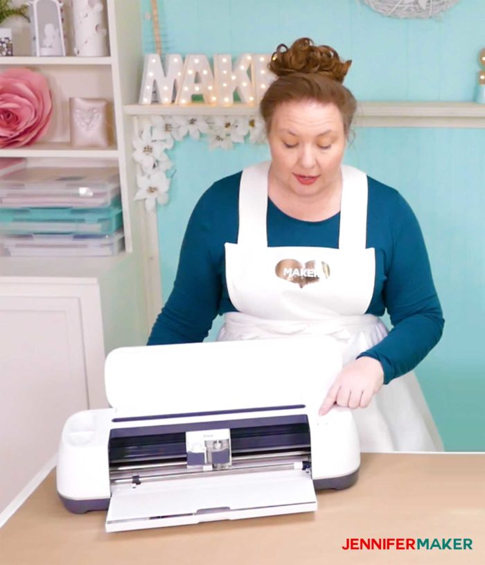 Jennifer Maker standing in front of her Cricut maker and showing how to make something