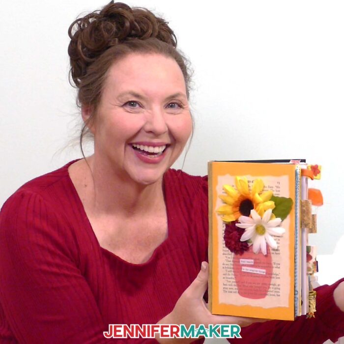 Jennifer Maker shows off a handmade junk journal decorated with paper flowers. Learn how to Make Junk Journals in the free tutorial