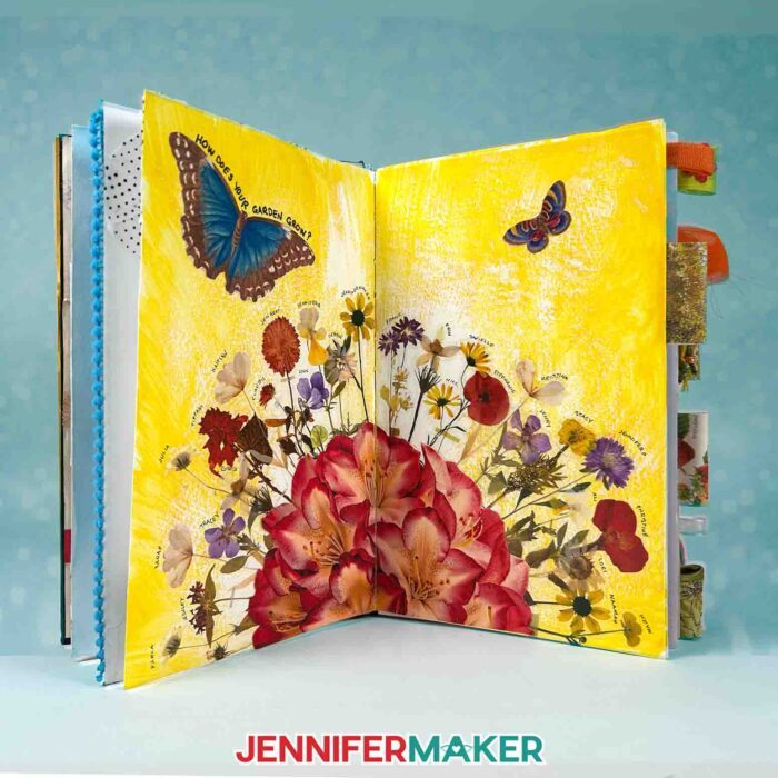 A junk journal sits open on a table, open and showing a spread inside with various butterfly and flower ephemera. Learn how to Make Junk Journals in the free tutorial