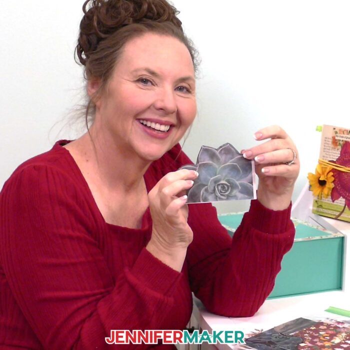 Jennifer Maker sits at her craft desk and shows off a piece of paper with a printed succulent on it that she can use to decorate her junk journal. Learn how to Make Junk Journals in the free tutorial