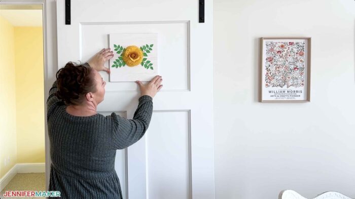 Jennifer positioning a lace paper flower sign on a door near other floral wall art.