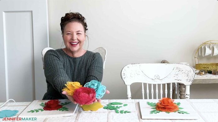 Jennifer at a table holding three colorful 3D assembled lace paper flowers.