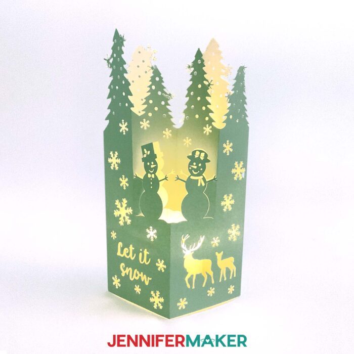 Make easy lantern pop-up cards with JenniferMaker's tutorial! A beautiful pop-up lantern cards with trees, snowmen, deer, and snowflakes with the message "Let It Snow" cut out, made from soft green cardstock stands up, lit from the inside by a battery-operated tealight candle.