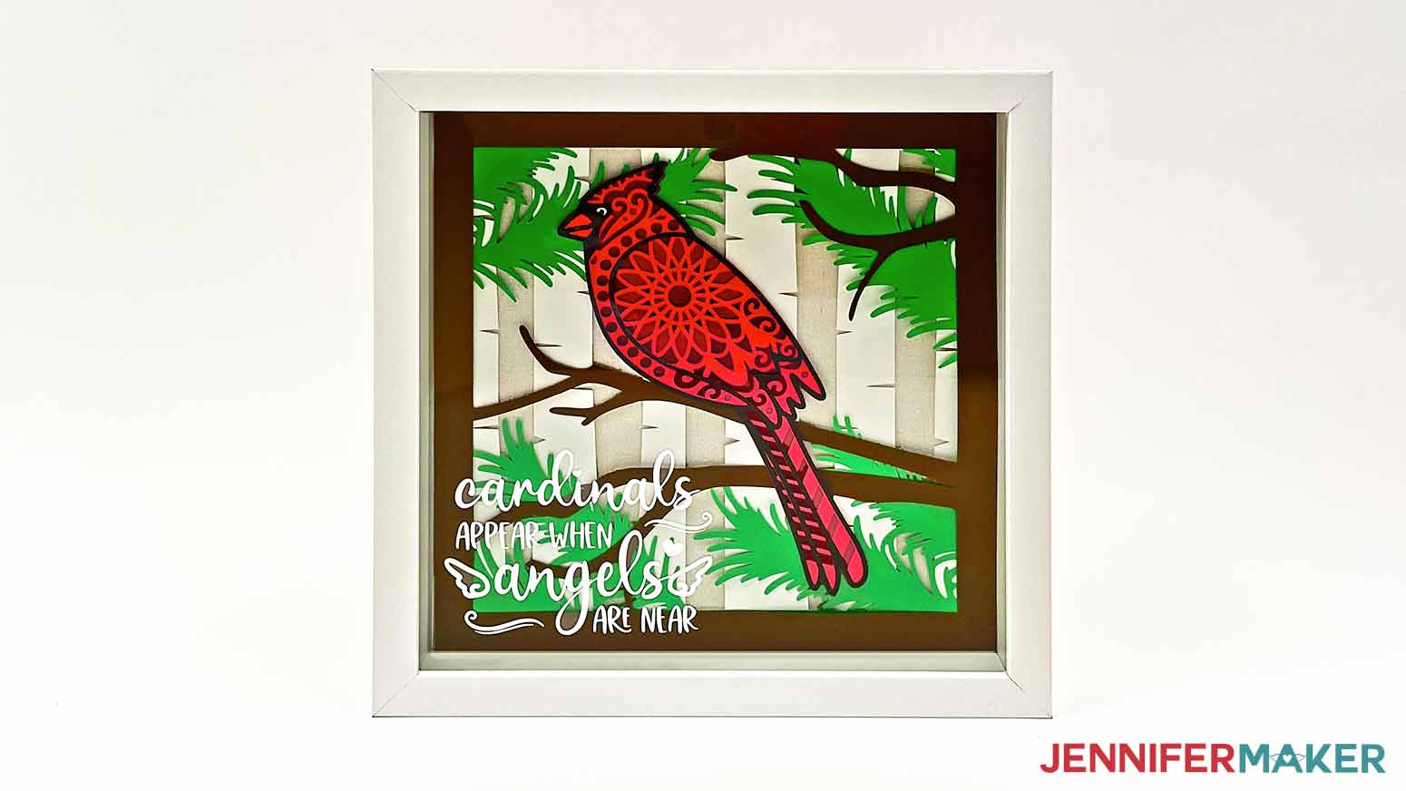 A photo of the finished layered cardinal svg project inside a shadow box with a white vinyl decal on the front of the glass