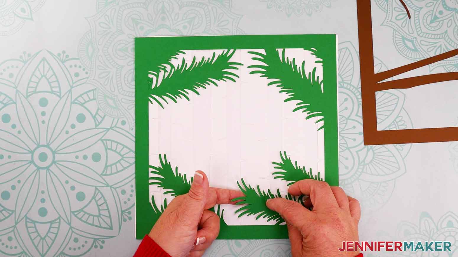 Two hands pointing to an overlapping area of the green pine needle and white birch tree background layers for the cardinal svg project