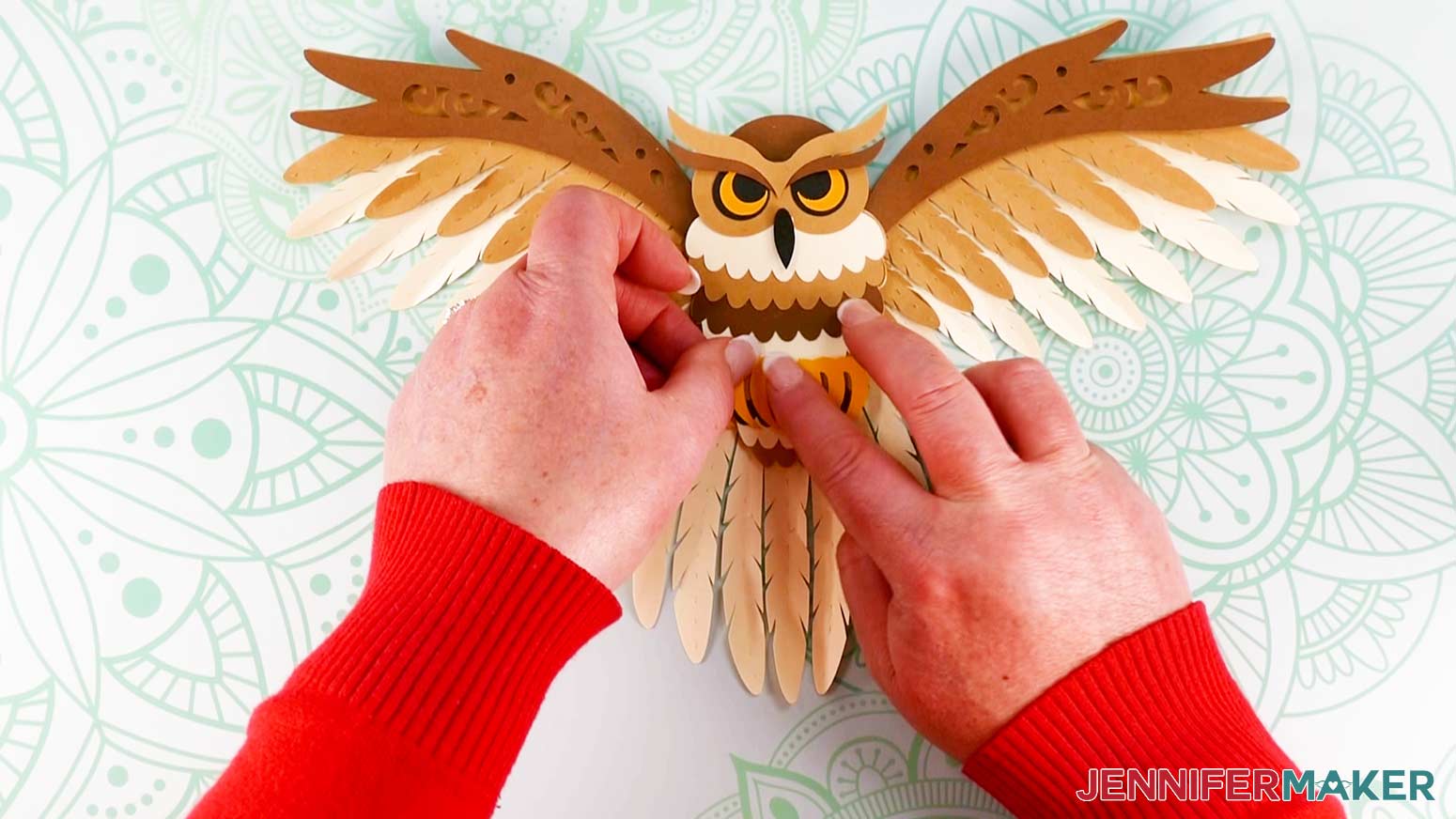 An overhead photo showing two hands pressing the small talon pieces onto the assembled layered owl on the work surface