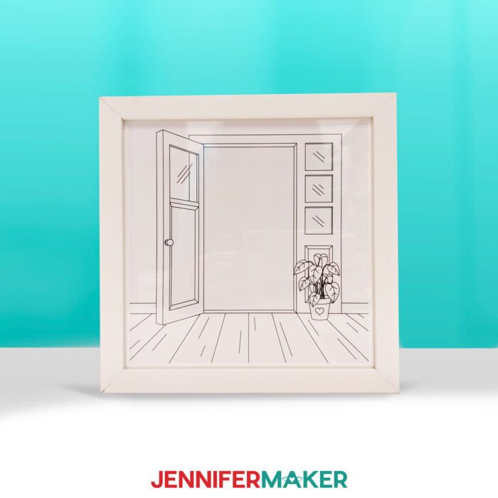 Make a light painting shadow box with JenniferMaker's tutorial! A shadowbox frame sits upon a table with a pretty blue backdrop. The shadowbox features a drawn doorway image. The light in the shadow box is off, hiding the photo inside.
