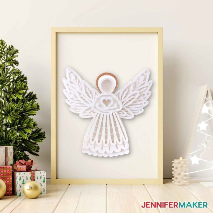 White paper angel inside frame next to mini Christmas trees