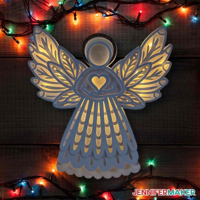 White paper angel illuminated with light background and Christmas lights