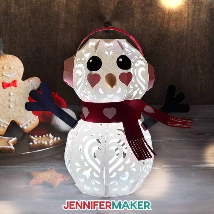 Light up snowman made of cardstock with earmuffs, a scarf, and cute facial details and heart design cutouts.