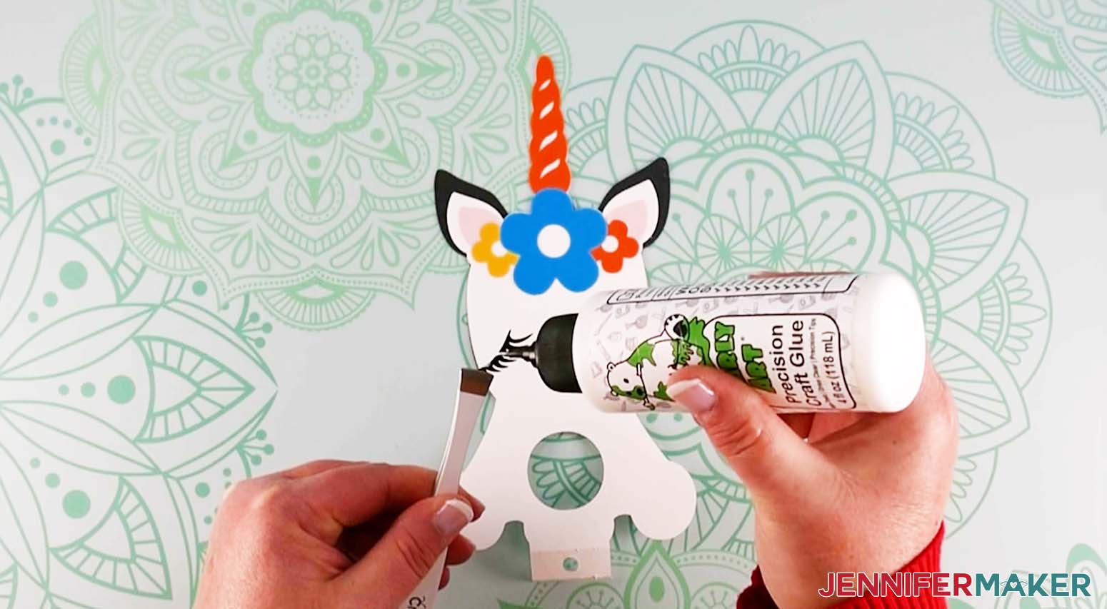 Crafter holding the unicorn's eyelash with tweezers while applying glue to attach it to the DIY lollipop holder.