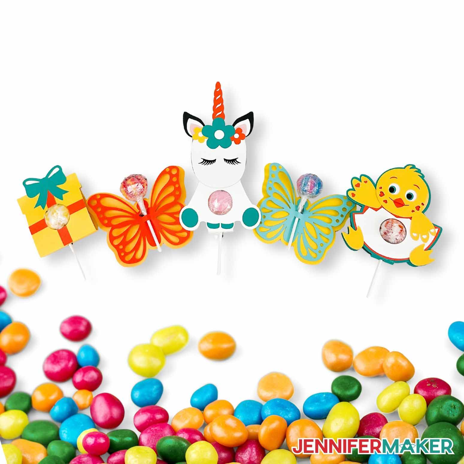 Present, unicorn, chick, and butterfly cardstock DIY lollipop holders on a white background surrounded by candy.