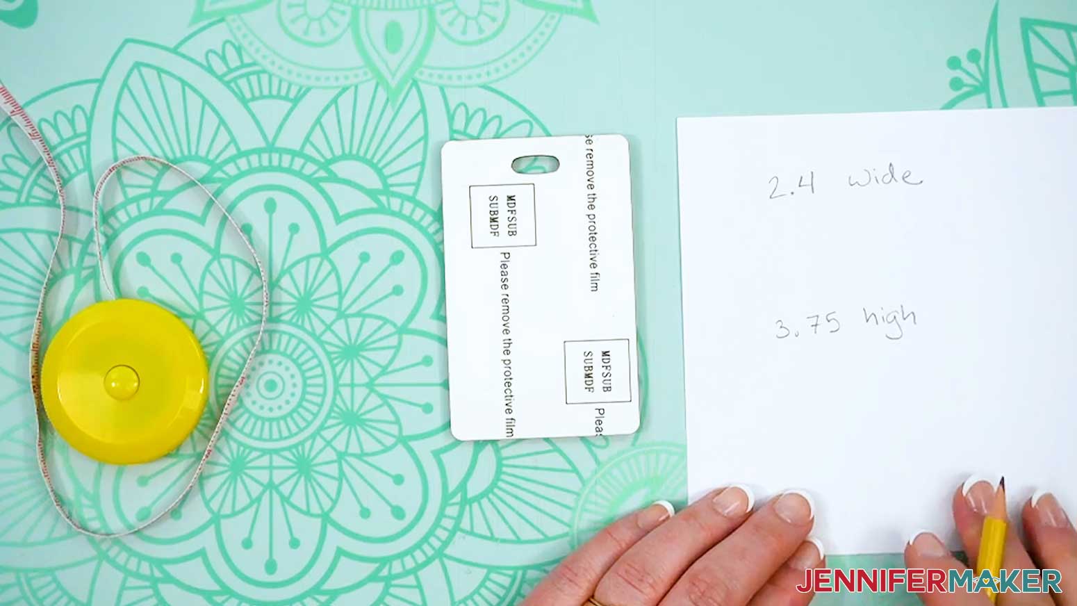 The blank dye sublimation tag is face down with the protective layer still on a piece of paper lists measurements and there is a measuring tape to the left of it.