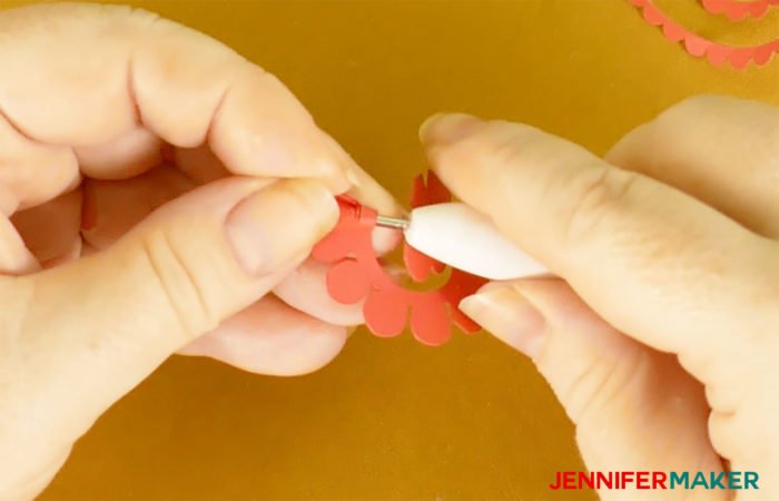 Rolling up a miniature paper rose around a quilling tool