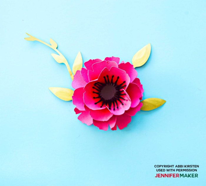 A finished pink paper poppy with a dark stamen and green leaves