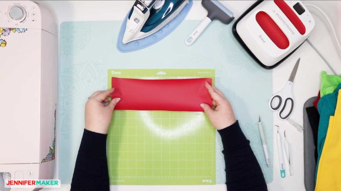 Place a red piece of iron on vinyl shiny side down on a green Cricut StandardGrip cutting mat to cut out an iron on design for a T-Shirt