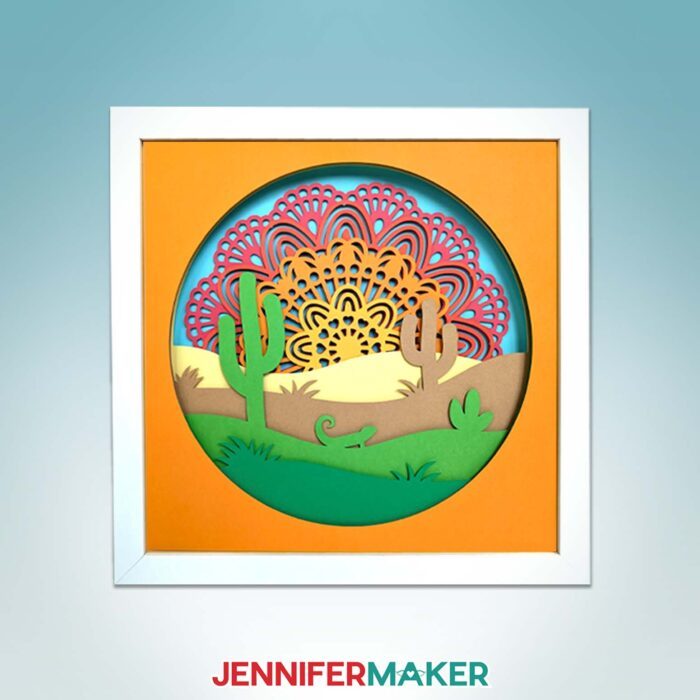 Get Jennifer Maker's best paper mandala tips! A cardstock mandala design featuring a sunset over the desert hangs on a blue backdrop.