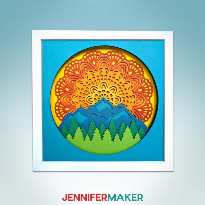 Get Jennifer Maker's best paper mandala tips! A cardstock mandala featuring a sunset over a forest hangs on a blue backdrop.