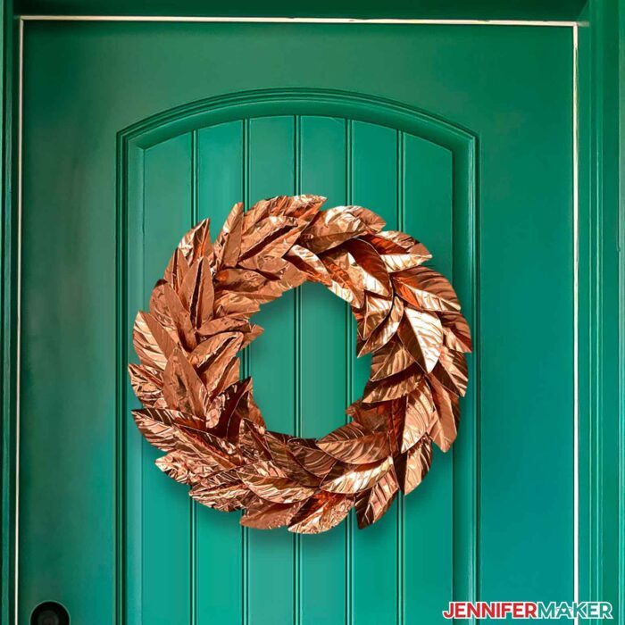 Coppery metal wreath with leaves cut on a Cricut hung on an emerald green front door.