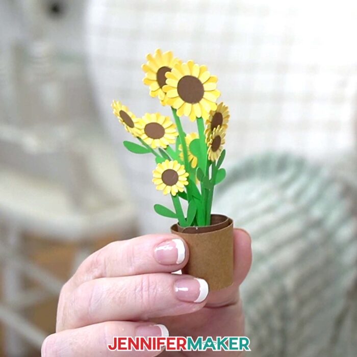 A hand holds a sunflower mini flower arrangement in a paper pot from JenniferMaker's Mini Paper Flower Tutorial