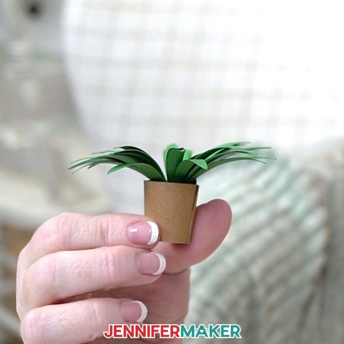 A hand holds a mini spider plant in a paper pot from JenniferMaker's Mini Paper Flower Tutorial