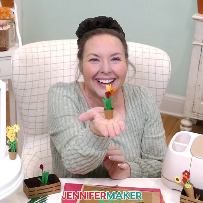 Jennifer Maker sits at her craft table, showing off a mini potted sunflower plant from her Mini Paper Flower Tutorial