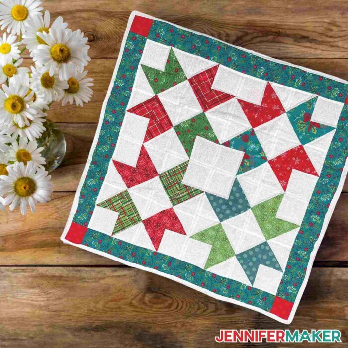 Mini quilt made using a Cricut machine on wooden background next to flowers