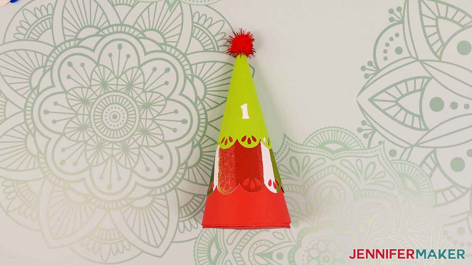 An assembled tree for the minimalist tree advent calendar, with a red pom pom on top and a white vinyl number 1 on the front.