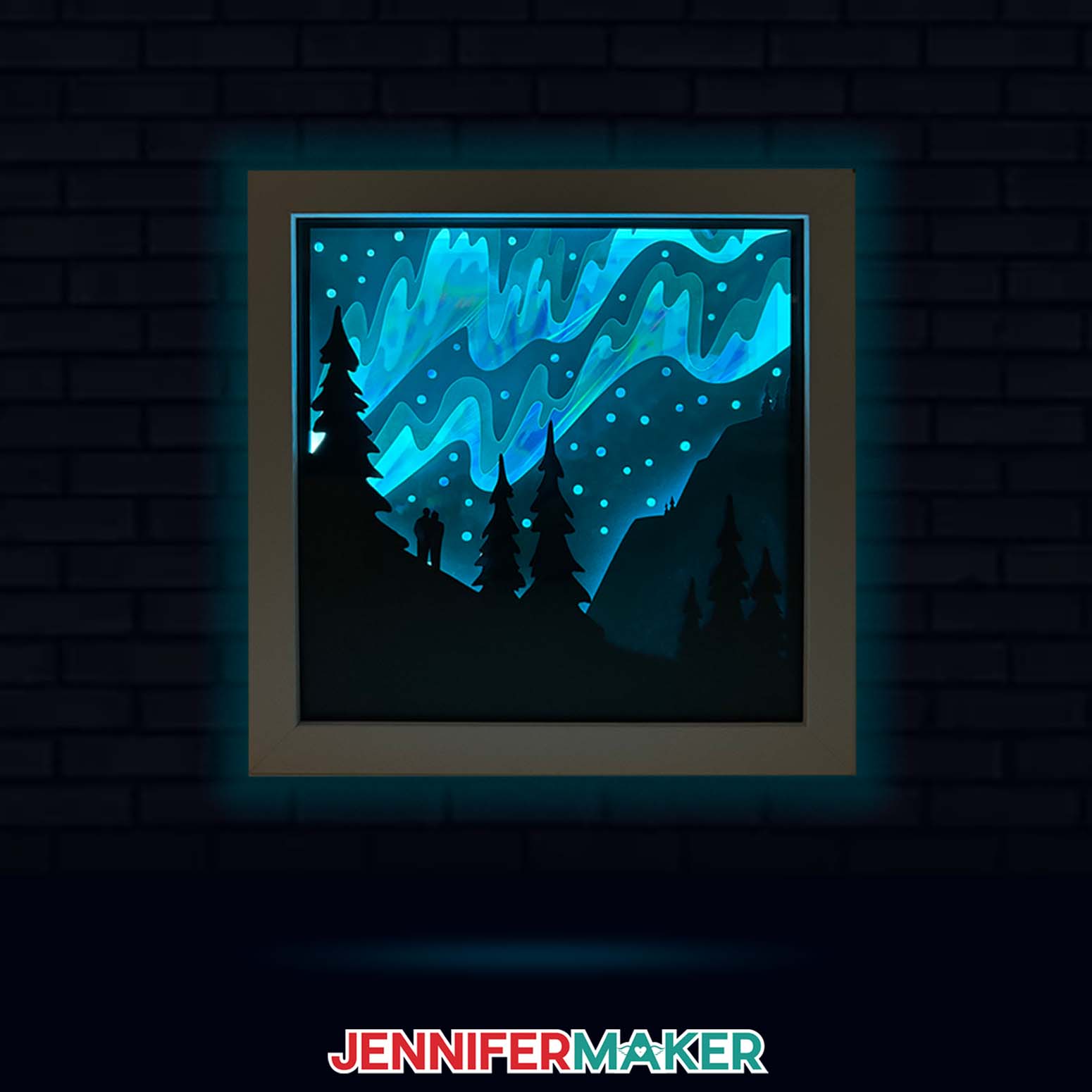 Learn to make a Northern Lights Shadow Box with JenniferMaker's tutorial! An illuminated cardstock shadow box featuring a glowing aurora borealis design is displayed on a dark brick wall.