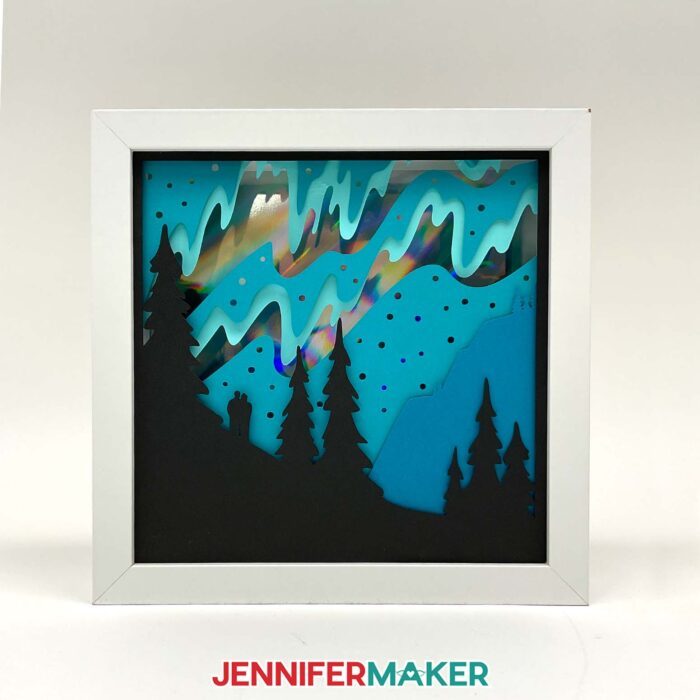 Northern Lights Shadow Box with holographic cardstock, in a white frame, sitting on a white surface