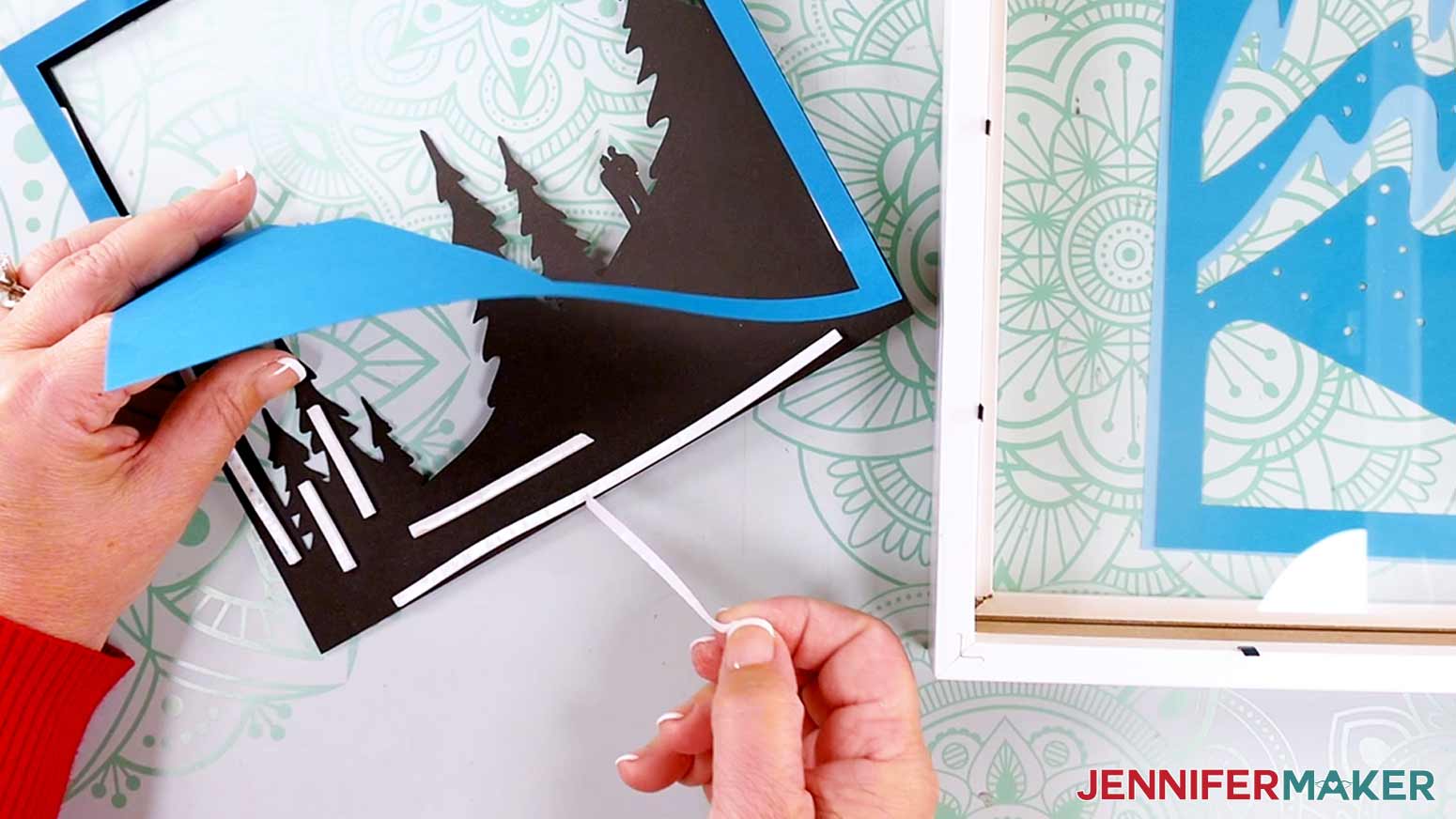 Peeling the backing off of the foam tape to adhere the layers in a Northern Lights Shadow Box