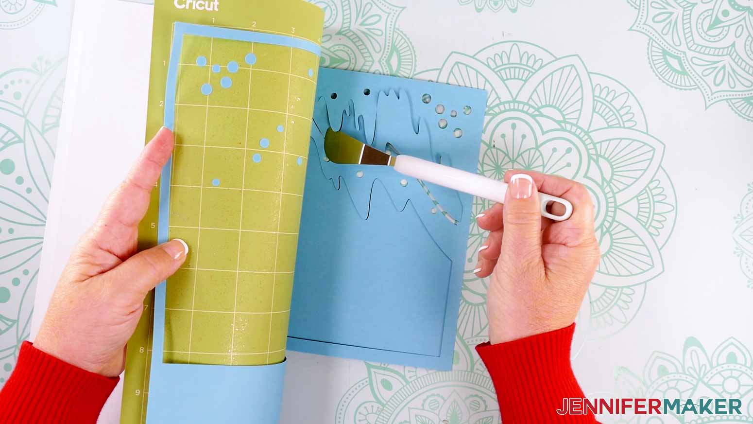 Using a spatula to remove the delicate cut cardstock pieces from the machine mat to make a customized Northern Lights Shadow Box