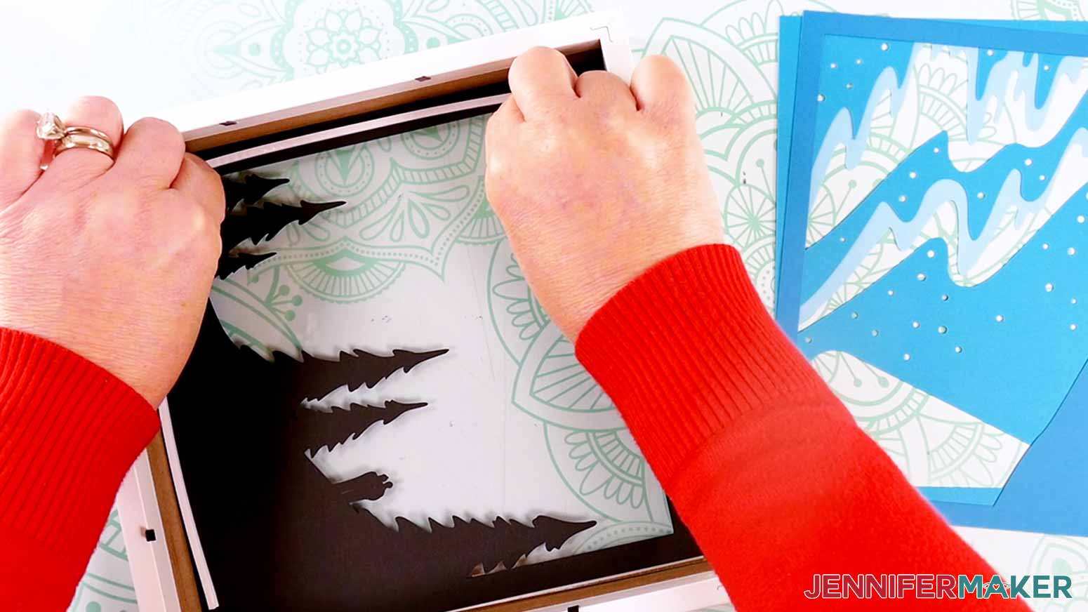 Adhering tape to the first layer of the cardstock design to make a customized Northern Lights Shadow Box
