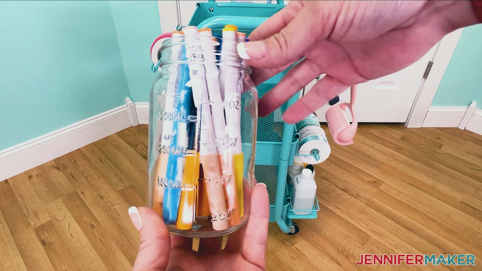 The Cricut pens are placed with the tip down in a glass mason jar.